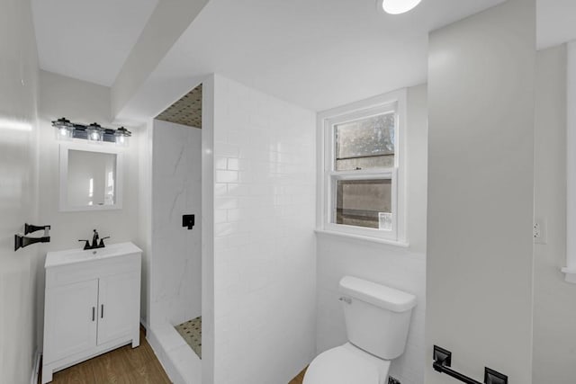 bathroom with toilet, wood-type flooring, vanity, and a tile shower