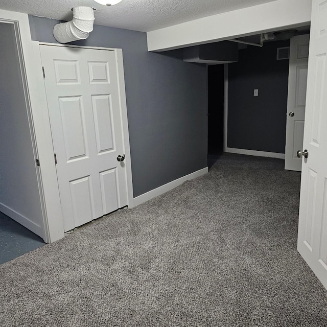 basement featuring a textured ceiling and dark carpet