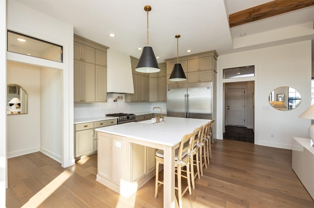 kitchen with a center island with sink, premium appliances, light hardwood / wood-style floors, and hanging light fixtures