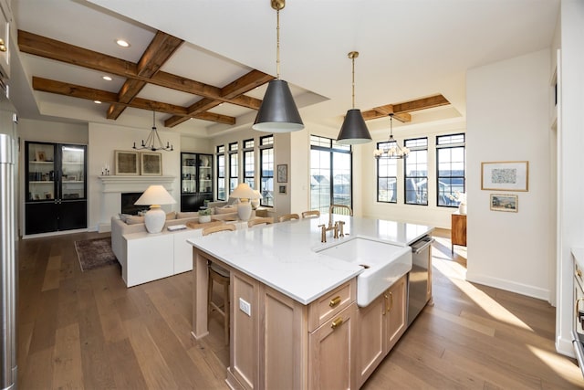 kitchen featuring sink, hardwood / wood-style flooring, an island with sink, light brown cabinetry, and decorative light fixtures