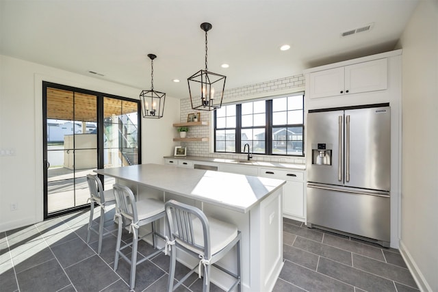 kitchen with stainless steel fridge, a kitchen breakfast bar, pendant lighting, white cabinets, and a center island