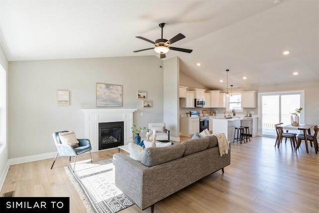 living room featuring ceiling fan, sink, high vaulted ceiling, and light wood-type flooring