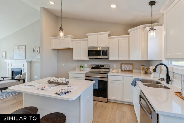 kitchen with stainless steel appliances, sink, light hardwood / wood-style flooring, white cabinets, and hanging light fixtures