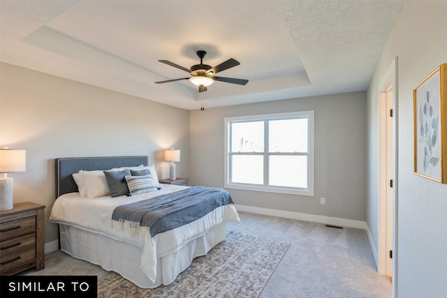 bedroom featuring ceiling fan, light colored carpet, a textured ceiling, and a tray ceiling