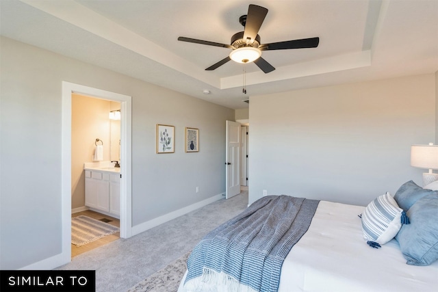 bedroom featuring a raised ceiling, light colored carpet, ensuite bath, and ceiling fan