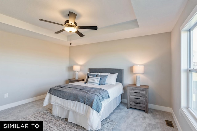 bedroom with ceiling fan, light carpet, and a tray ceiling