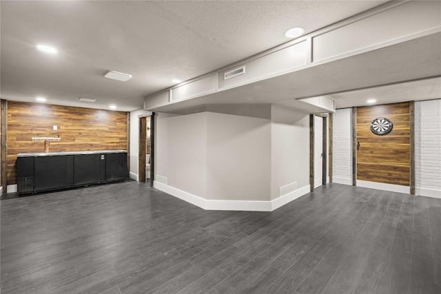 basement featuring dark wood-type flooring, wooden walls, and a textured ceiling