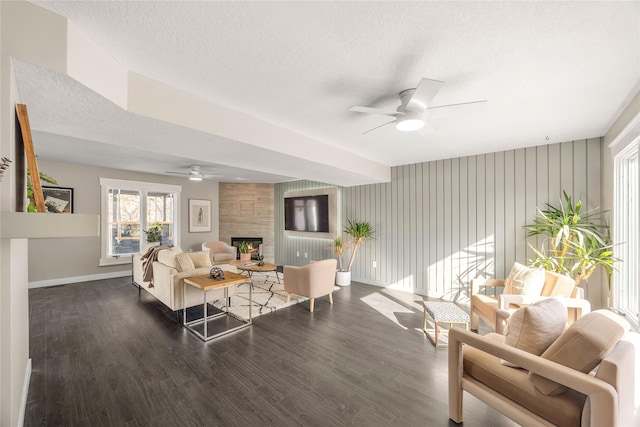 living room with a large fireplace, dark wood-type flooring, a textured ceiling, and ceiling fan