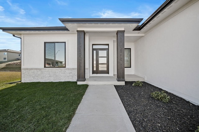 view of exterior entry with a yard, stucco siding, and stone siding