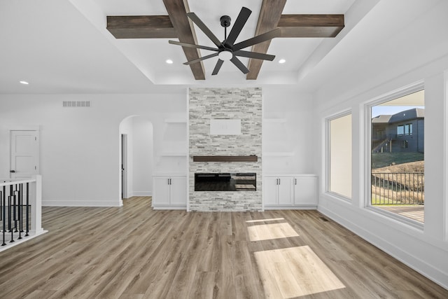 unfurnished living room with a stone fireplace, ceiling fan, beamed ceiling, and light hardwood / wood-style floors