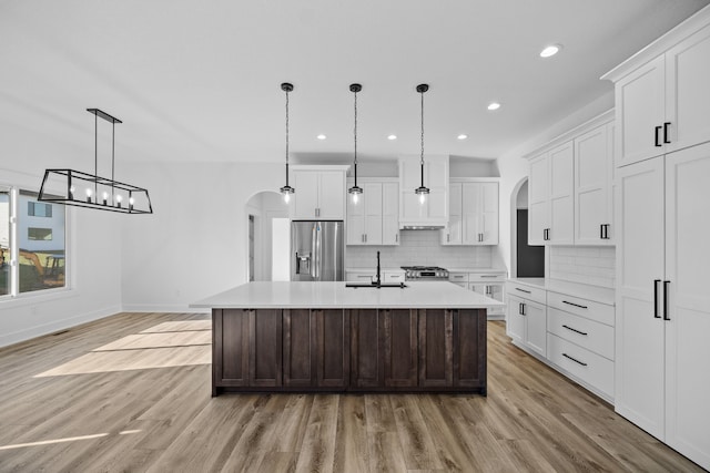 kitchen with appliances with stainless steel finishes, pendant lighting, a center island with sink, light hardwood / wood-style flooring, and white cabinetry