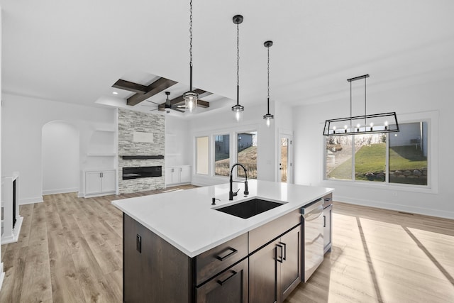 kitchen with dishwasher, sink, an island with sink, dark brown cabinets, and light hardwood / wood-style floors