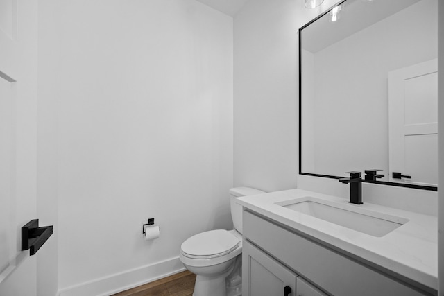bathroom with wood finished floors, toilet, vanity, and baseboards