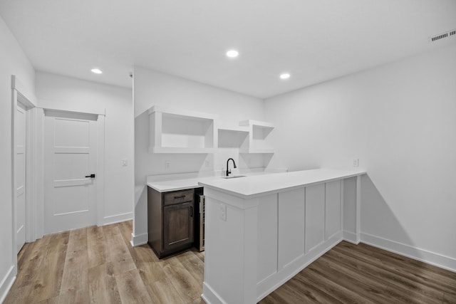 kitchen featuring kitchen peninsula, sink, dark brown cabinetry, and light wood-type flooring