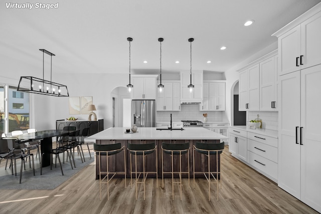 kitchen featuring arched walkways, stainless steel refrigerator with ice dispenser, a sink, decorative backsplash, and recessed lighting
