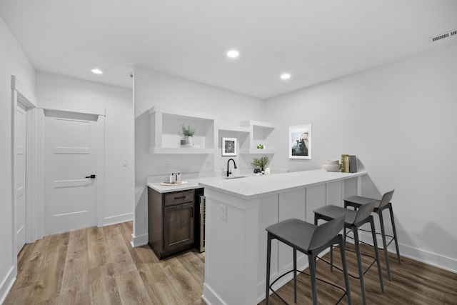 kitchen with open shelves, a breakfast bar area, light countertops, light wood-style flooring, and recessed lighting