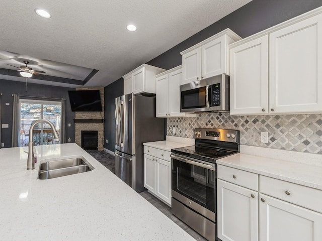 kitchen featuring white cabinets, stainless steel appliances, a stone fireplace, and sink