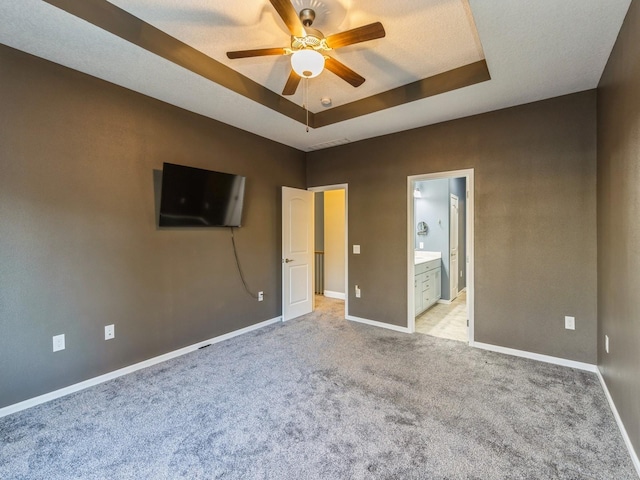 unfurnished bedroom featuring ensuite bathroom, a textured ceiling, light colored carpet, a tray ceiling, and ceiling fan