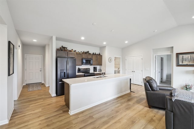 kitchen with appliances with stainless steel finishes, light wood-type flooring, dark brown cabinetry, vaulted ceiling, and a center island with sink