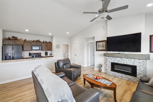 living room with ceiling fan, a stone fireplace, sink, and light hardwood / wood-style flooring