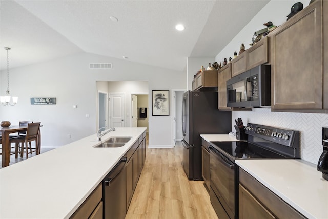 kitchen with vaulted ceiling, sink, black appliances, decorative light fixtures, and light hardwood / wood-style floors