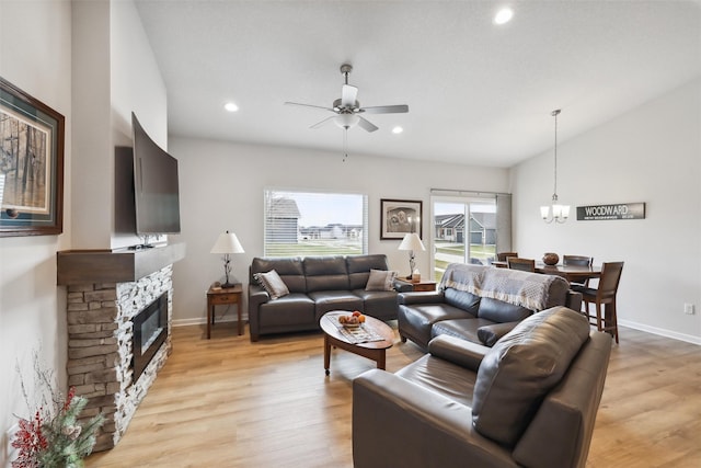 living room featuring vaulted ceiling, a stone fireplace, light hardwood / wood-style floors, and ceiling fan with notable chandelier