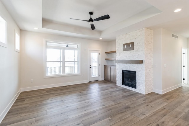 unfurnished living room with wood finished floors, visible vents, baseboards, a fireplace, and a raised ceiling