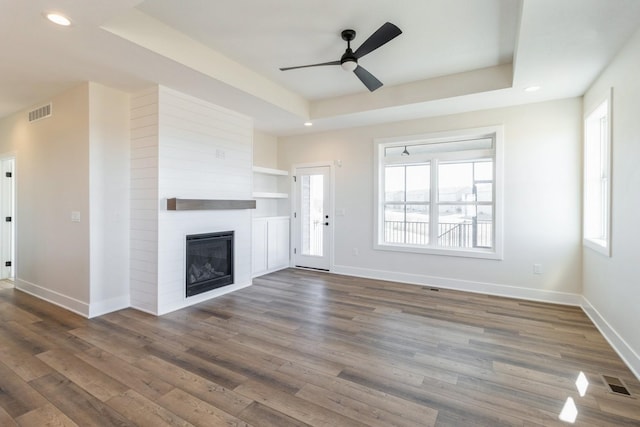 unfurnished living room with a raised ceiling, dark wood-style floors, visible vents, and baseboards