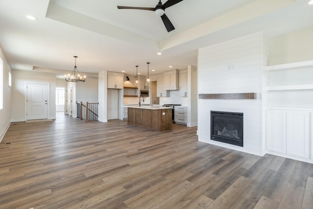 unfurnished living room featuring a raised ceiling, recessed lighting, wood finished floors, and a sink