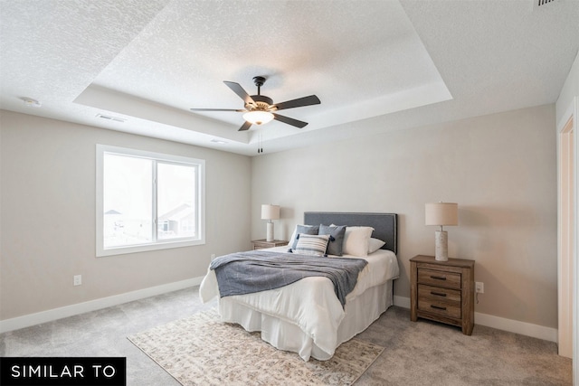 bedroom featuring a textured ceiling, light colored carpet, a raised ceiling, and ceiling fan