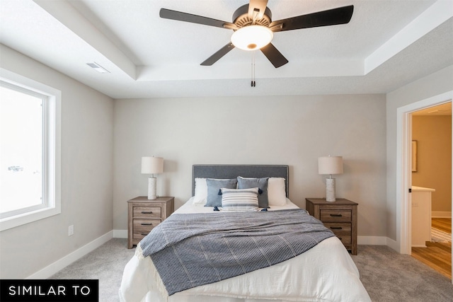 bedroom featuring ceiling fan, light colored carpet, and a tray ceiling