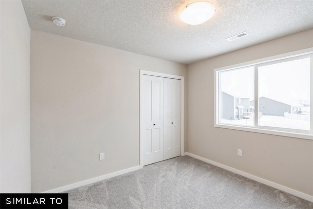 unfurnished bedroom featuring light colored carpet, a textured ceiling, and a closet