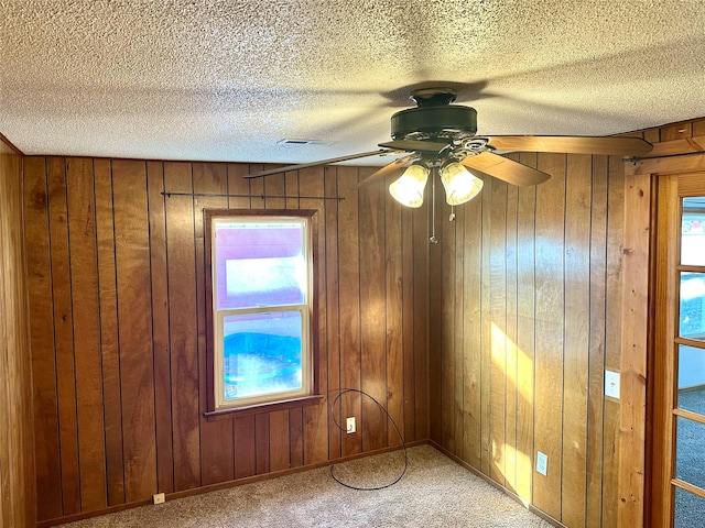 carpeted spare room with ceiling fan, a textured ceiling, plenty of natural light, and wood walls