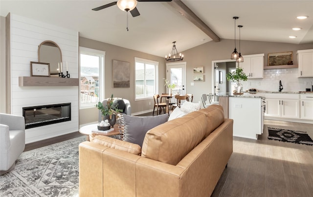 living room featuring a large fireplace, sink, lofted ceiling with beams, wood-type flooring, and ceiling fan with notable chandelier