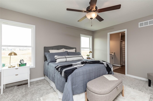 carpeted bedroom featuring ceiling fan, a textured ceiling, connected bathroom, and multiple windows