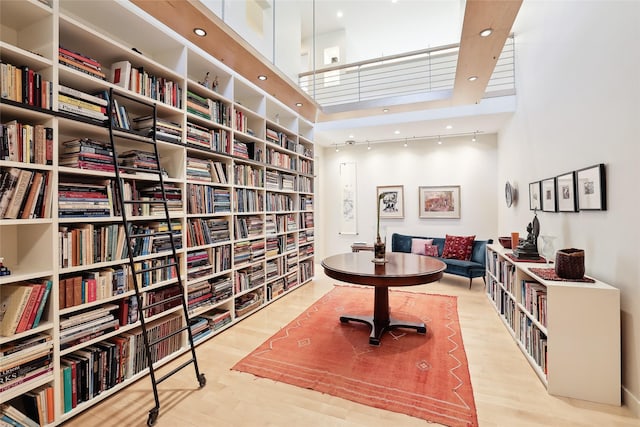 living area with light wood-style floors, track lighting, bookshelves, and a high ceiling