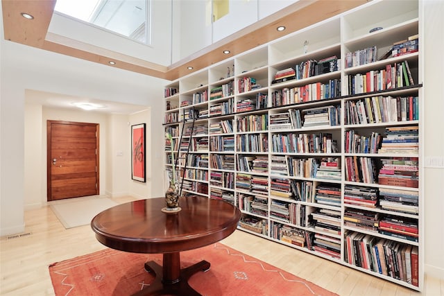 sitting room with bookshelves, a high ceiling, wood finished floors, and visible vents