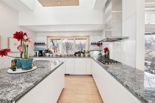 kitchen with stainless steel gas stovetop, stone countertops, white cabinets, a sink, and exhaust hood