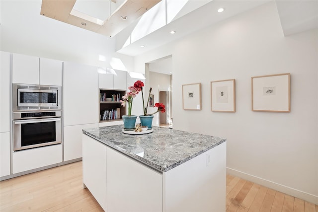 kitchen featuring light stone countertops, light wood-style floors, white cabinets, appliances with stainless steel finishes, and a center island