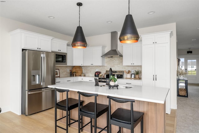 kitchen with white cabinets, an island with sink, wall chimney exhaust hood, and appliances with stainless steel finishes