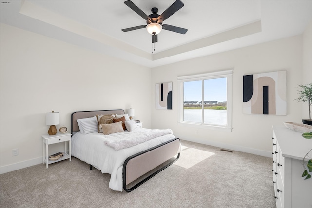 carpeted bedroom with a raised ceiling and ceiling fan