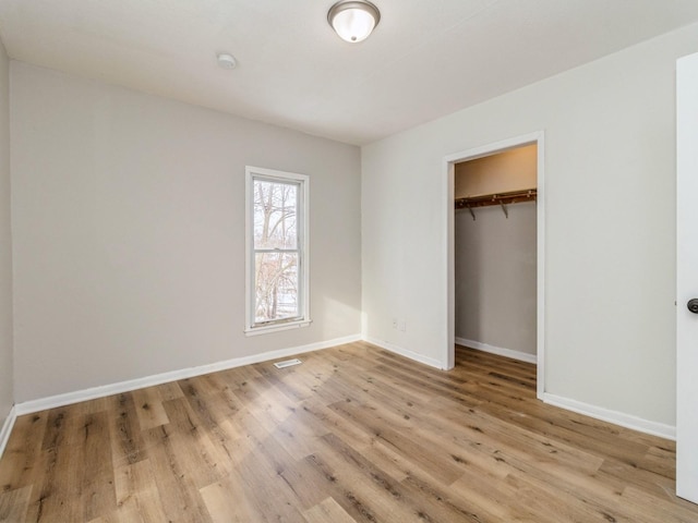 unfurnished bedroom with a closet, a spacious closet, and light hardwood / wood-style flooring