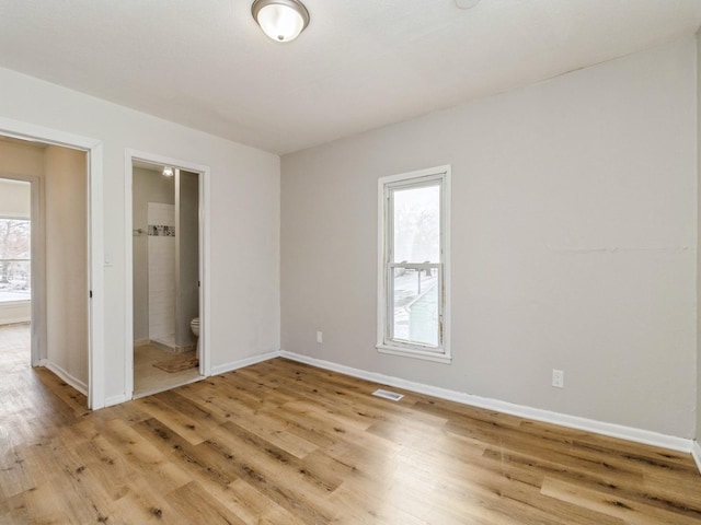 unfurnished bedroom featuring ensuite bath, light hardwood / wood-style flooring, and multiple windows