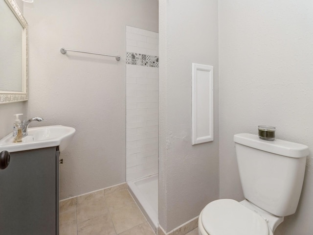 bathroom with tiled shower, vanity, tile patterned flooring, and toilet