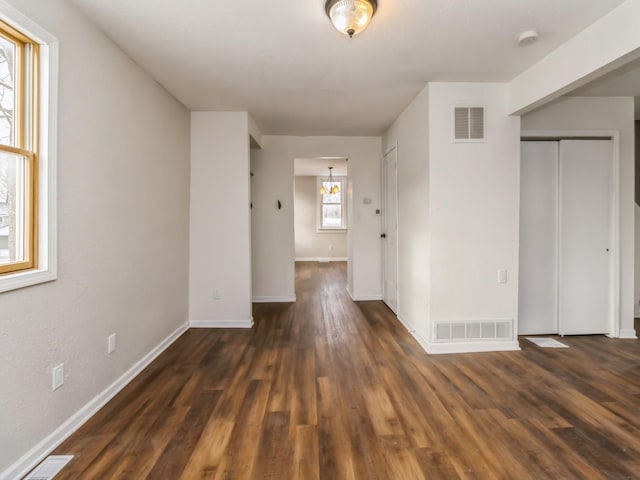 spare room featuring dark hardwood / wood-style floors, an inviting chandelier, and plenty of natural light