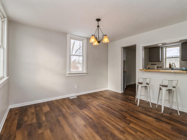 interior space with plenty of natural light, dark hardwood / wood-style floors, a kitchen bar, and decorative light fixtures