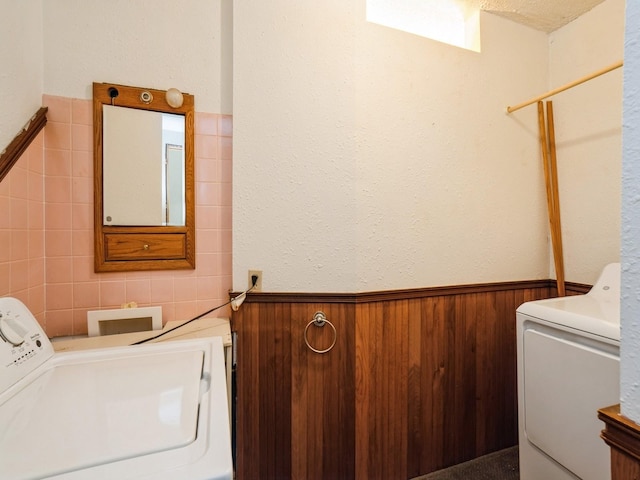 clothes washing area with a textured ceiling, washing machine and dryer, tile walls, and wooden walls