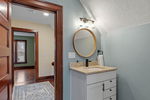 bathroom featuring vanity, a textured ceiling, vaulted ceiling, and wood-type flooring