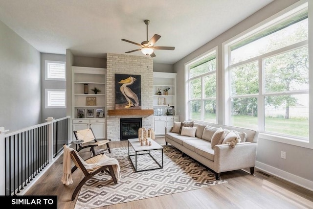 living room featuring built in shelves, ceiling fan, light hardwood / wood-style floors, and a brick fireplace