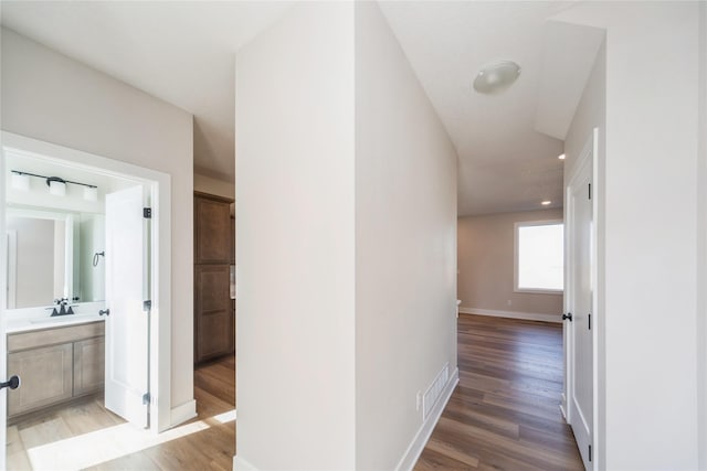 hallway featuring visible vents, a sink, light wood-style flooring, and baseboards